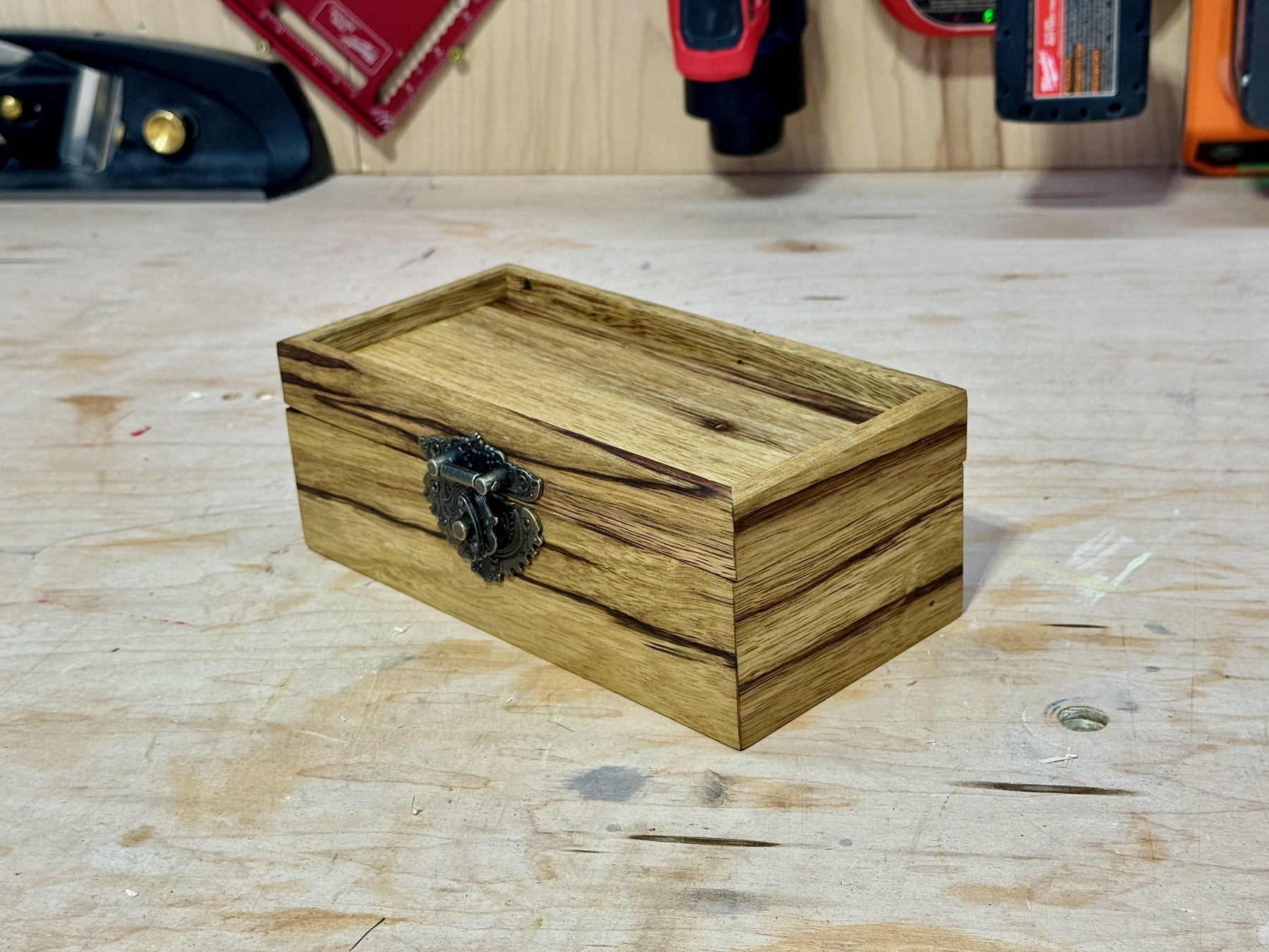 A small wooden box with a decorative metal latch rests on a wooden surface in a workshop setting.